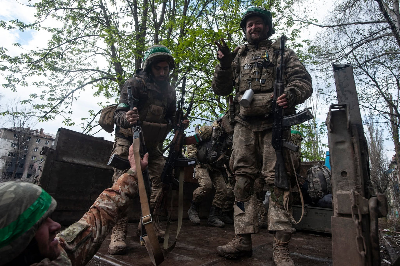 Servicemembers beside a vehicle under trees.
